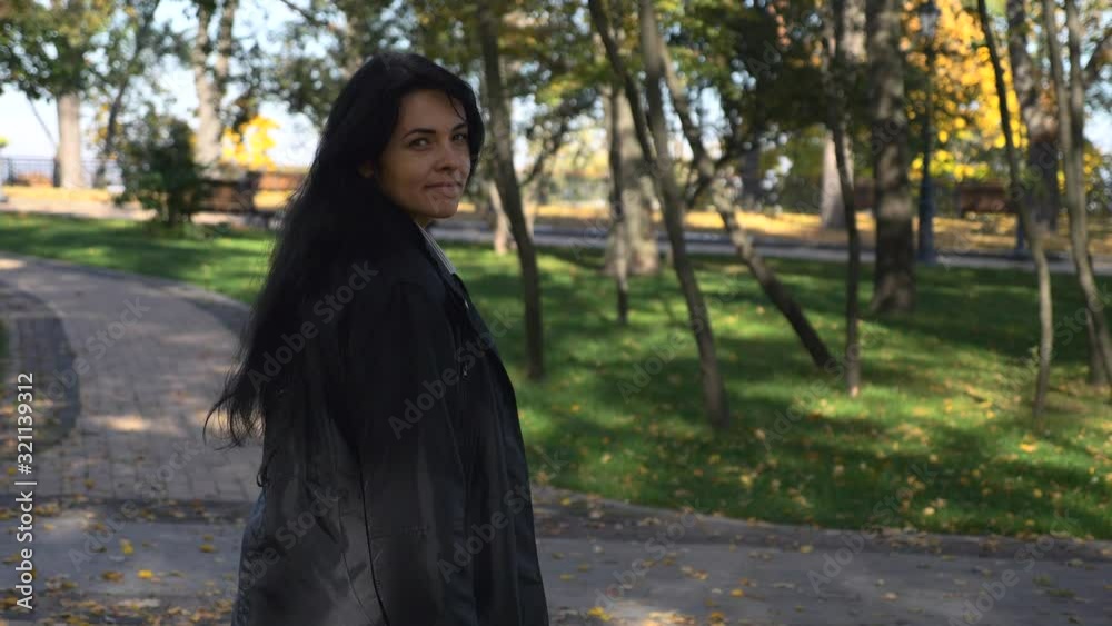 Camera Follows Beautiful Serious Girl Looks Back And Smiles Walking In The City Park And Thinking. Morning In City Park. Autumn Sunny Day. 4K Slow Motion 60 fps