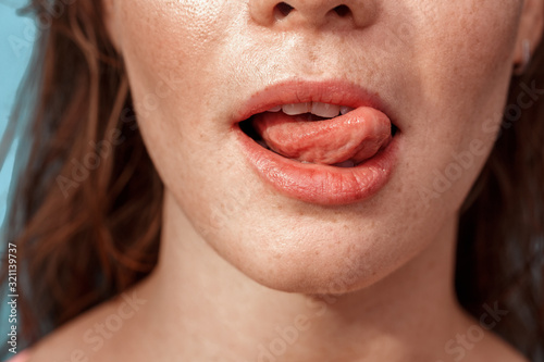 Summer Freestyle. Young woman with freckles standing isolated on blue showing tongue playful close-up