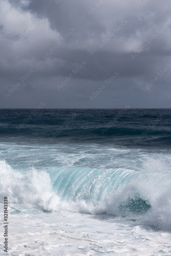 Kaimu Beach, Hawaii, USA. - January 14, 2020: Portrait of Dark ocean under heavy gray rain cloudscape produces white surf when azure wave turns and crashes.