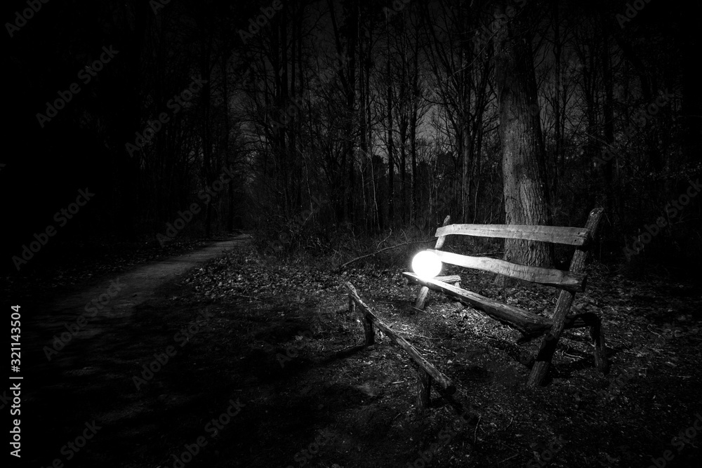 Orbe, source de lumière ronde sur une vieux banc en bois  au milieu d'une forêt - Mystère et peur dans l'obscurité - Magie et ésotérisme dans la nuit - Noir et blanc