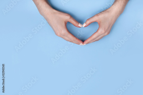 Female hands show a heart symbol on a light blue background. Place for text  copy space.