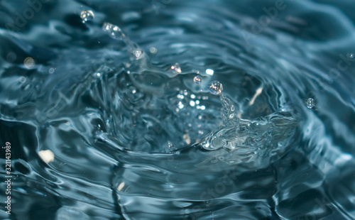 Conceptual image for water purity. Blue water splash   ed for background. Drops and waves in a glass.