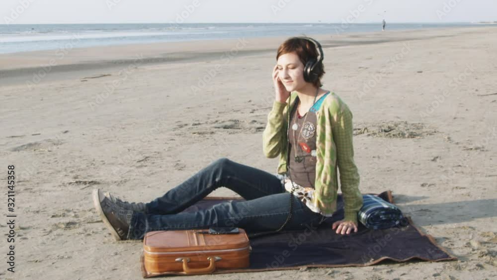 WS, Lockdown of a woman sitting on the beach listening to headphones WS, Lockdown of a woman sitting on the beach listening to headphones