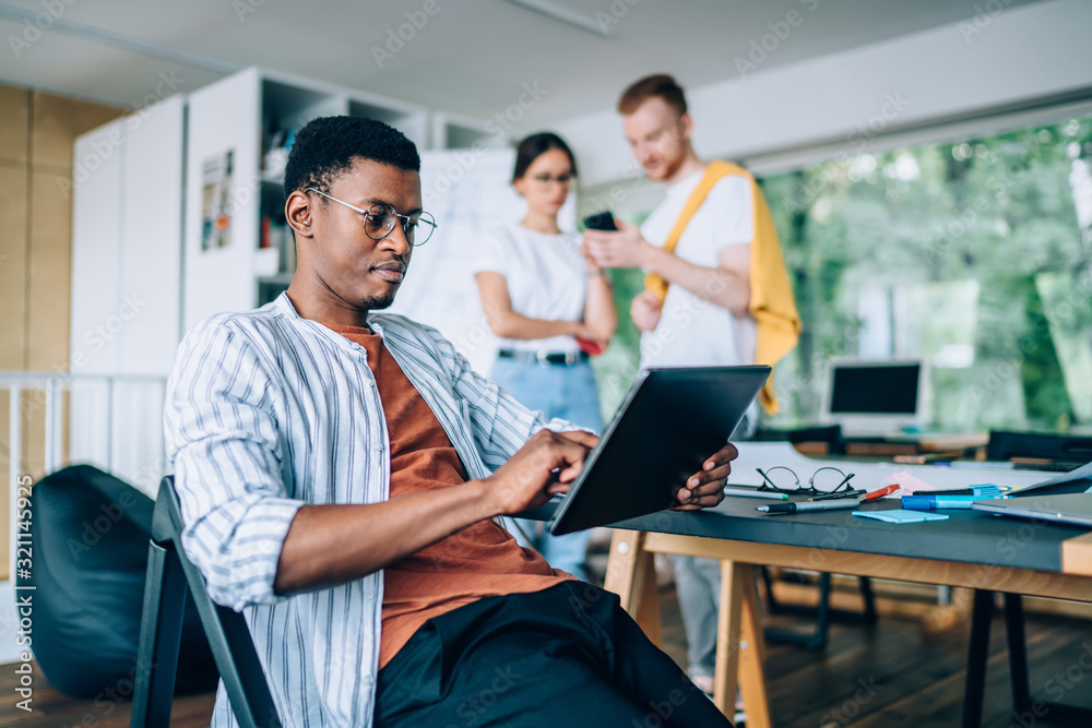 Focused black student browsing tablet in library