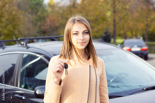 Closeup portrait serious young attractive woman, buyer near her new car showing keys isolated outside dealer, dealership lot office. Personal transportation, auto purchase concept © hbrh