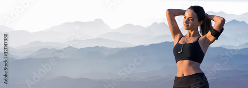 A thin athletic girl takes a break between classes on the background of mountains in the early morning, enjoys silence and freedom.