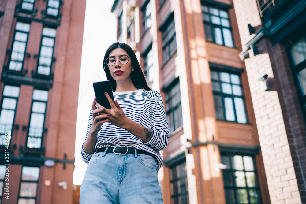 Fototapeta premium Millennial female blogger using 4g tariff with unlimited internet access for networking social websites and sharing content news to followers, Latino woman in classic glasses texting via application