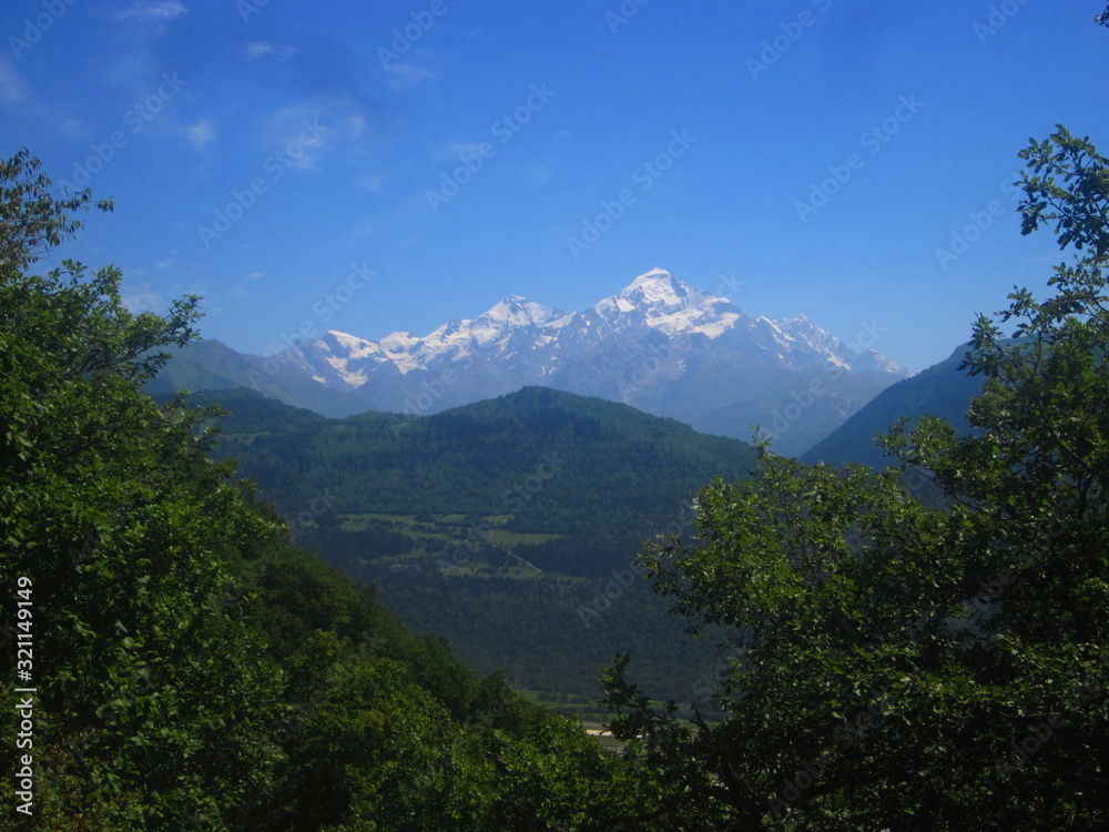 Mountain landscape of Svaneti on bright summer sunny day. Mountain lake, hills covered green grass on snowy rocky mountains background. Caucasus peaks in Georgia. Amazing view on wild georgian nature Mountain landscape of Svaneti on bright summer sunny day. Mountain lake, hills covered green grass on snowy rocky mountains background. Caucasus peaks in Georgia. Amazing view on wild georgian nature