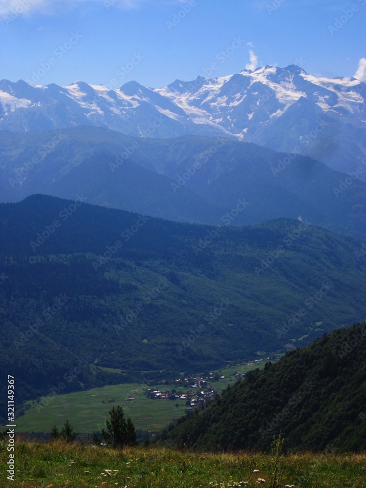 Mountain landscape of Svaneti on bright summer sunny day. Mountain lake, hills covered green grass on snowy rocky mountains background. Caucasus peaks in Georgia. Amazing view on wild georgian nature