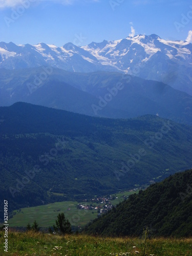 Mountain landscape of Svaneti on bright summer sunny day. Mountain lake  hills covered green grass on snowy rocky mountains background. Caucasus peaks in Georgia. Amazing view on wild georgian nature