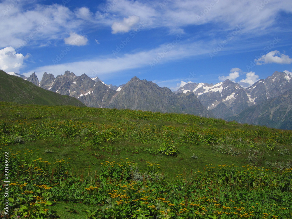 Mountain landscape of Svaneti on bright summer sunny day. Mountain lake, hills covered green grass on snowy rocky mountains background. Caucasus peaks in Georgia. Amazing view on wild georgian nature