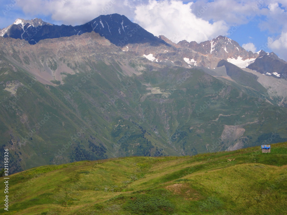 Mountain landscape of Svaneti on bright summer sunny day. Mountain lake, hills covered green grass on snowy rocky mountains background. Caucasus peaks in Georgia. Amazing view on wild georgian nature