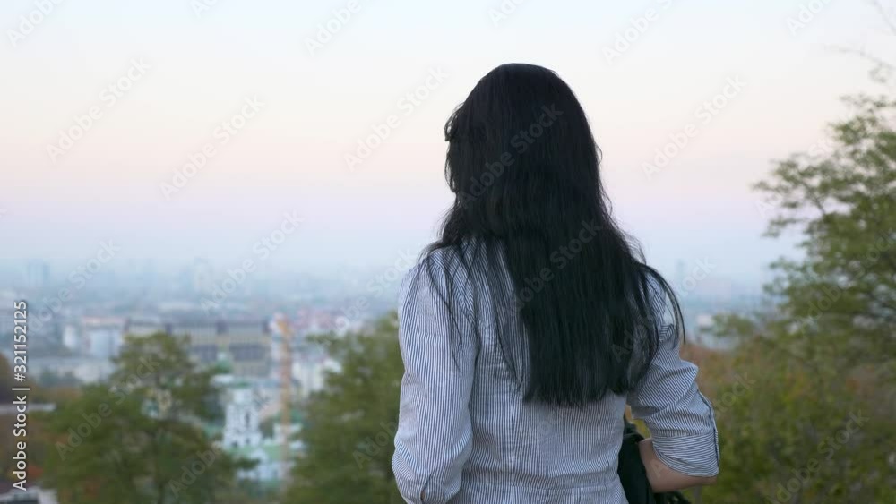 Beautiful Girl Standing And Thinking In The City Park On The Hill. Looking On Evening (Morning) Sky Above Cityscape. Summer Autumn Season Beautiful Girl Standing And Thinking In The City Park On The Hill. Looking On Evening (Morning) Sky Above Cityscape. Summer Autumn Season