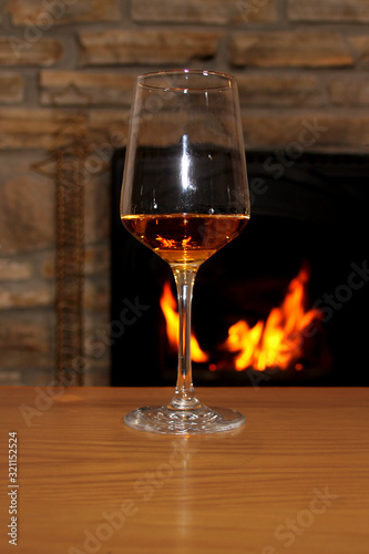 one glass of wine stands on a table in front of a fireplace, in which firewood burns with a bright flame