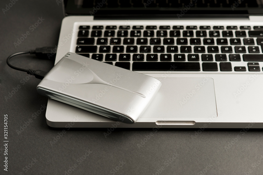 aluminum external hard drive with cable (usb) connected to laptop, on black office table.Top view aluminum external hard drive with cable (usb) connected to laptop, on black office table.Top view