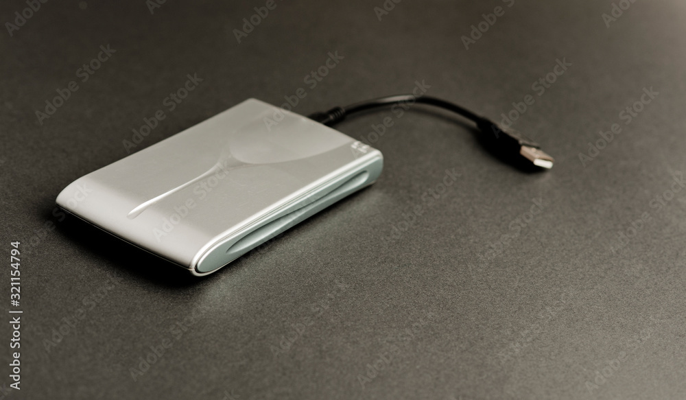 External hard drive aluminum with connection cable (USB), dark gray background.