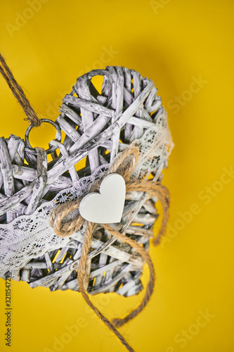 gray decorative heart made of branches with woolen thread. Vesid jewelry pendant over a yellow background. Valentine's Day