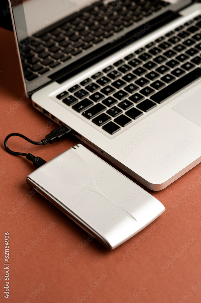 Aluminum external hard drive, partial laptop view, brown background, office concept. Aluminum external hard drive, partial laptop view, brown background, office concept.