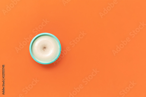Top view on a bright jar of turquoise color with cosmetic cream on an orange background. The concept of beauty, medicine, facial and body skin care, hair care