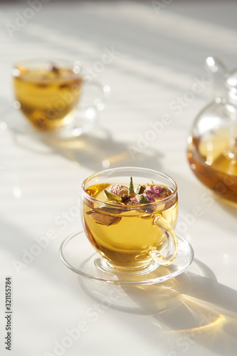 Cup of rose tea on abstract background of natural curtain shadow falling on white table, in rays of sunlight. Minimalism concept for design. Sunny summer day. Copy space.