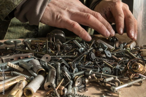 Man with rough hands is looking for in a pile of old nuts, bolts, screws, angles and other metal pieces