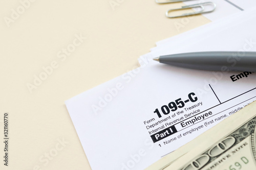 IRS Form 1095-C Employer-Provided Health Insurance Offer and Coverage tax blank lies with pen and many hundred dollar bills on calendar page photo