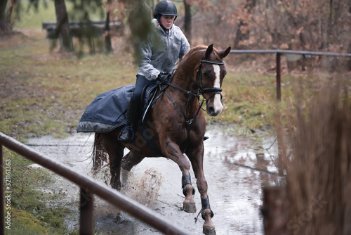 Reiterin galoppiert in der Vielseitigkeit mit ihrem Pferd durch einen Wassergraben