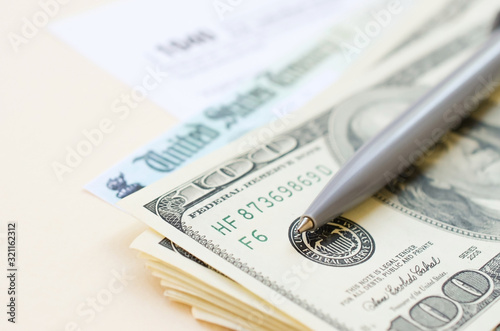 1040 Individual Income tax return form with Refund Check and hundred dollar bills on beige background