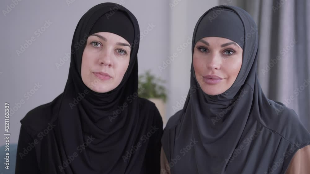 Close-up of conservative and modern-looking Muslim women looking at camera and smiling. Two different ladies from one culture posing indoors. Lifestyle, beauty, diversity. Close-up of conservative and modern-looking Muslim women looking at camera and smiling. Two different ladies from one culture posing indoors. Lifestyle, beauty, diversity.