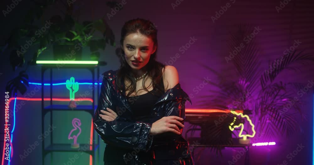 Portrait shot of young brunette Caucasian attractive female model striking poses like professional on neon lights decorations on background. Beautiful woman moving seductively. Indoor club atmosphere. Portrait shot of young brunette Caucasian attractive female model striking poses like professional on neon lights decorations on background. Beautiful woman moving seductively. Indoor club atmosphere.
