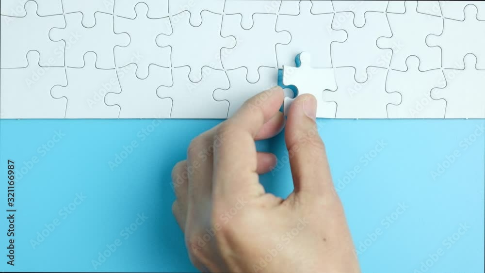 Hand putting the last piece of white jigsaw puzzle on blue background and place for your content Hand putting the last piece of white jigsaw puzzle on blue background and place for your content
