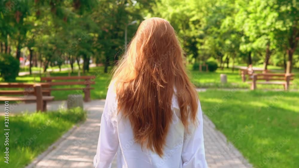 redhead female in white elegant shirt walk on the street surrounded green trees and grass slow motion redhead female in white elegant shirt walk on the street surrounded green trees and grass slow motion
