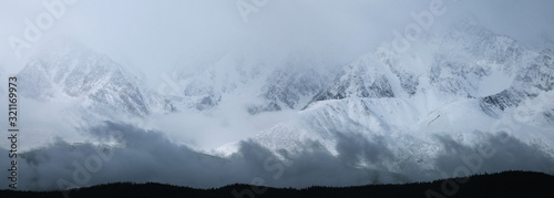 Bad weather in the mountains, clouds, fog. Panoramic view of a snowy ridge. Traveling in the mountains, climbing.