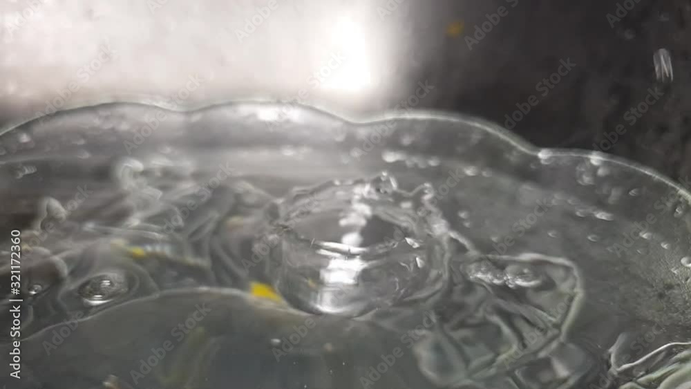 Faucet drainage hole in stainless kitchen sink with water dripping and splashing droplets in crystal floral pattern bowl in slow motion. Faucet drainage hole in stainless kitchen sink with water dripping and splashing droplets in crystal floral pattern bowl in slow motion.