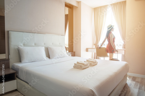 Tourist woman standing nearly window with her luggage in hotel bedroom.