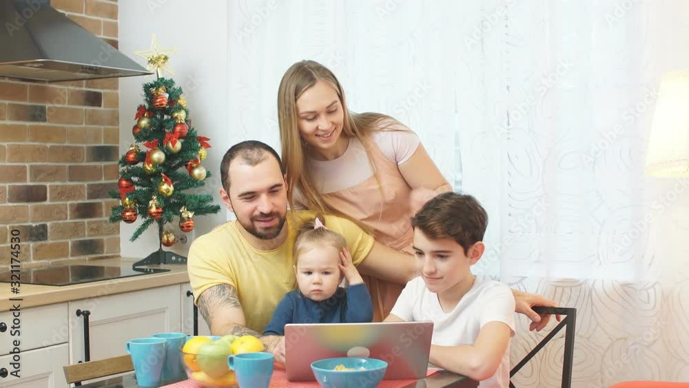 Kids and parents in casual wear in modern kitchen, have meal and watching video on modern laptop. Love and family concept. Kids and parents in casual wear in modern kitchen, have meal and watching video on modern laptop. Love and family concept.
