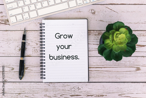 Plakat Grow your business text on notepad on top of wooden table, with computer keyboard, pen and potted plant