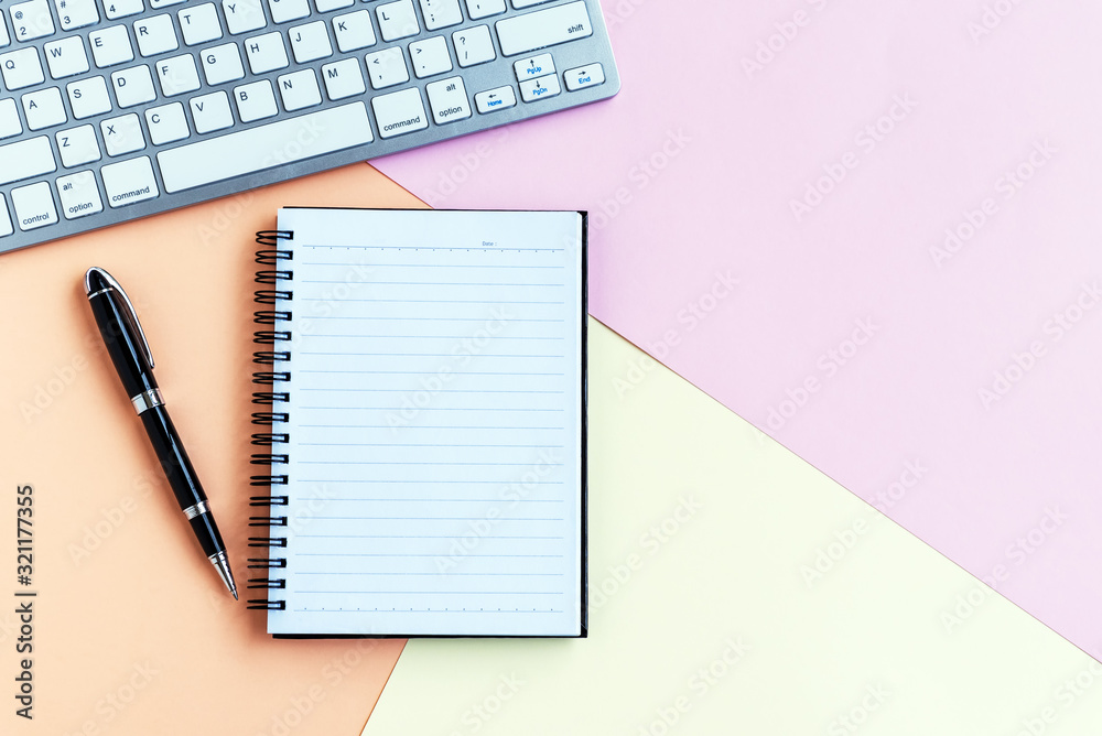 Notepad, pen, computer keyboard on top of pastel colored background Notepad, pen, computer keyboard on top of pastel colored background