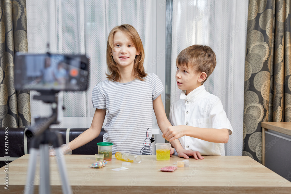 Naklejka premium Cute little bloggers with homemade slime recording vlog video on kitchen.