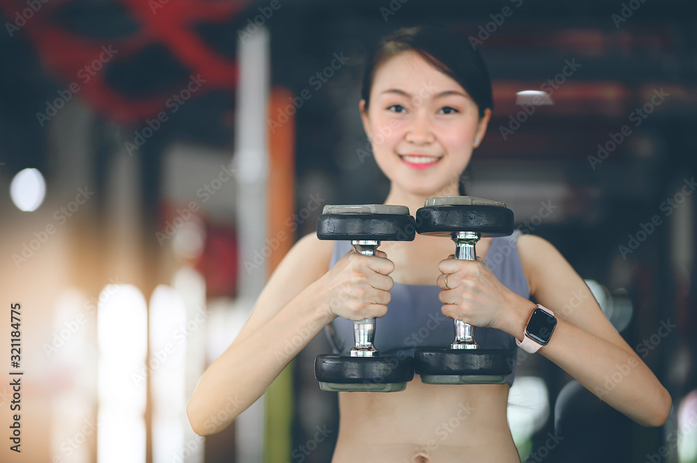 Young fitness woman holding dumbbells and workout at gym.