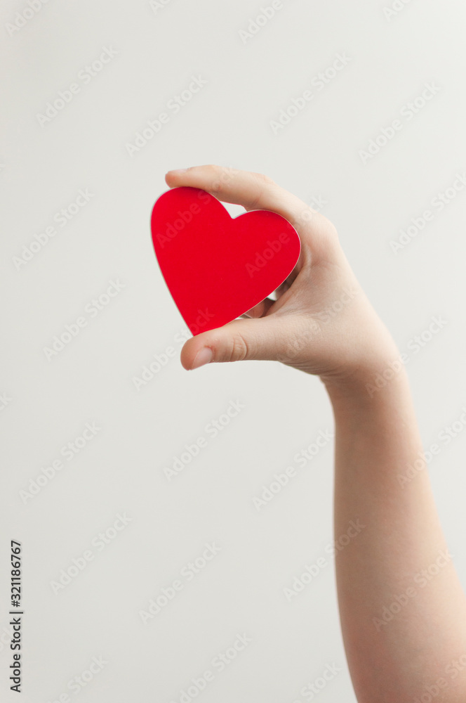 Fototapeta premium Child's hand holding red heart over white background
