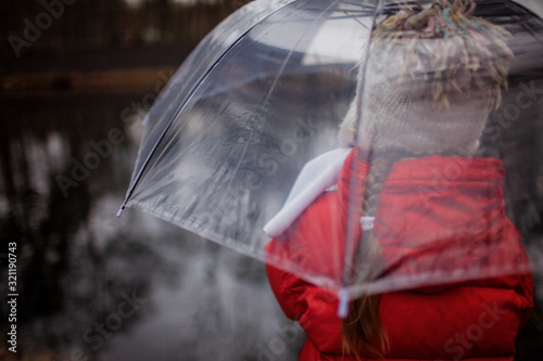 Fototapeta Naklejka Na Ścianę i Meble -  7-8 years girl in red coat with transparent umbrella walking alone in spring forest
