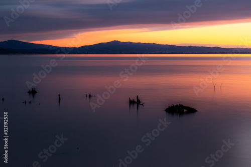 Sunset a Trasimeno lake (Umbria, Italy), with fishing net poles and branches on perfectly still water