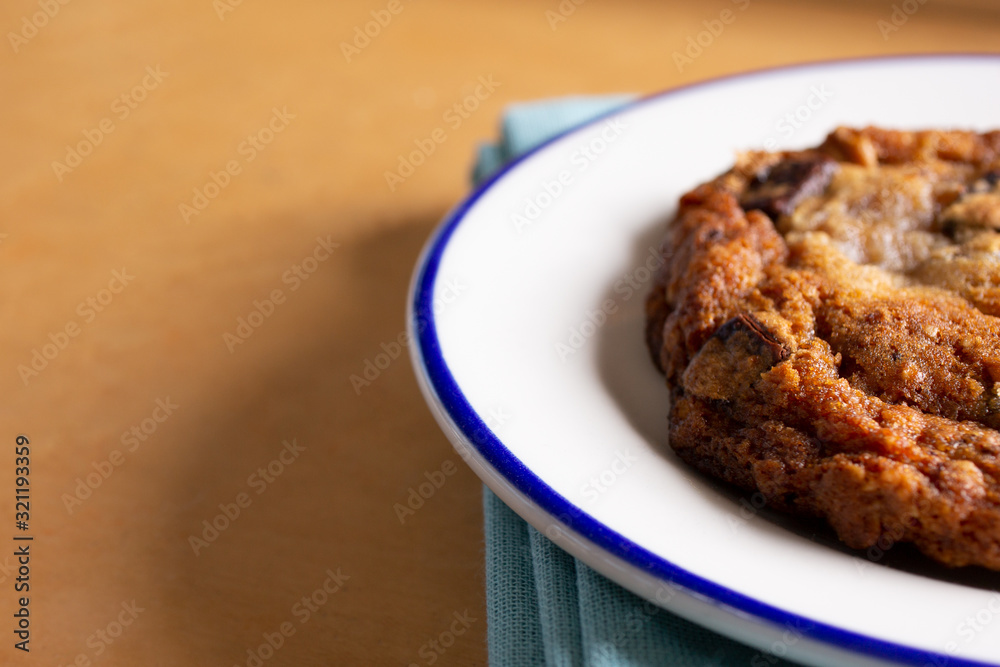 A view of chocolate chip cookie on a plate in a restaurant or kitchen setting, sitting on the right side of the frame.