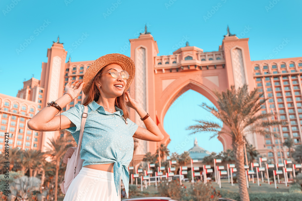 Happy indonesian girl traveler relaxing near famous luxury Atlantis hotel building on a Jumeirah Palm Island in Duba, UAE