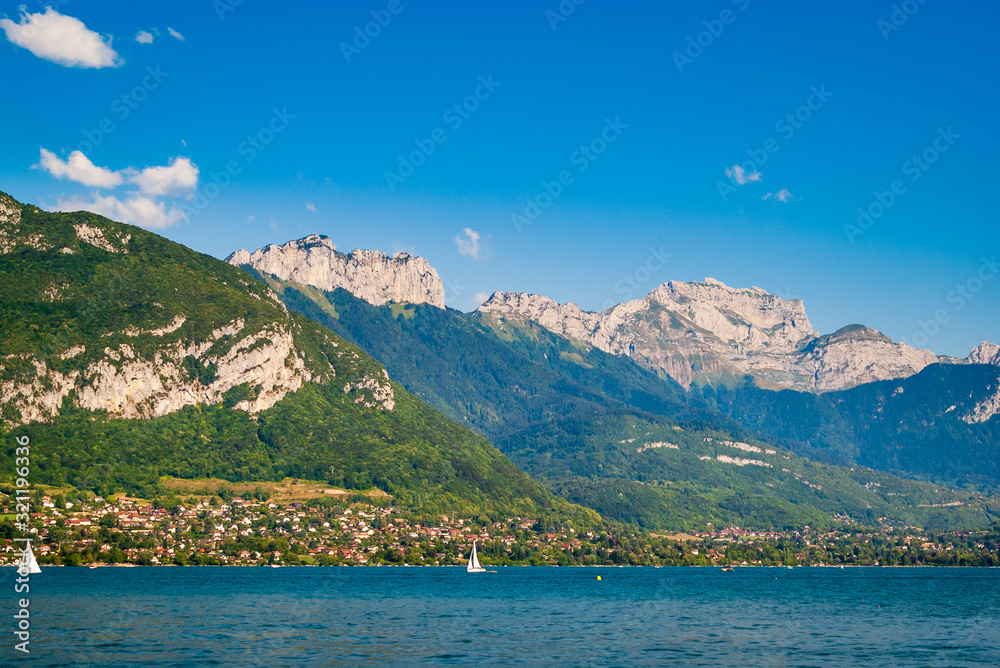A summer view of the beautiful French Lake Annecy with its turquoise crystal clear waters surrounded by stunning mountains, Savoy, France.
