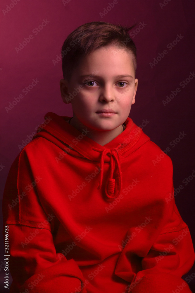 Studio portrait of a dark-haired boy, on a maroon background, in a red hoodie jacket Studio portrait of a dark-haired boy, on a maroon background, in a red hoodie jacket
