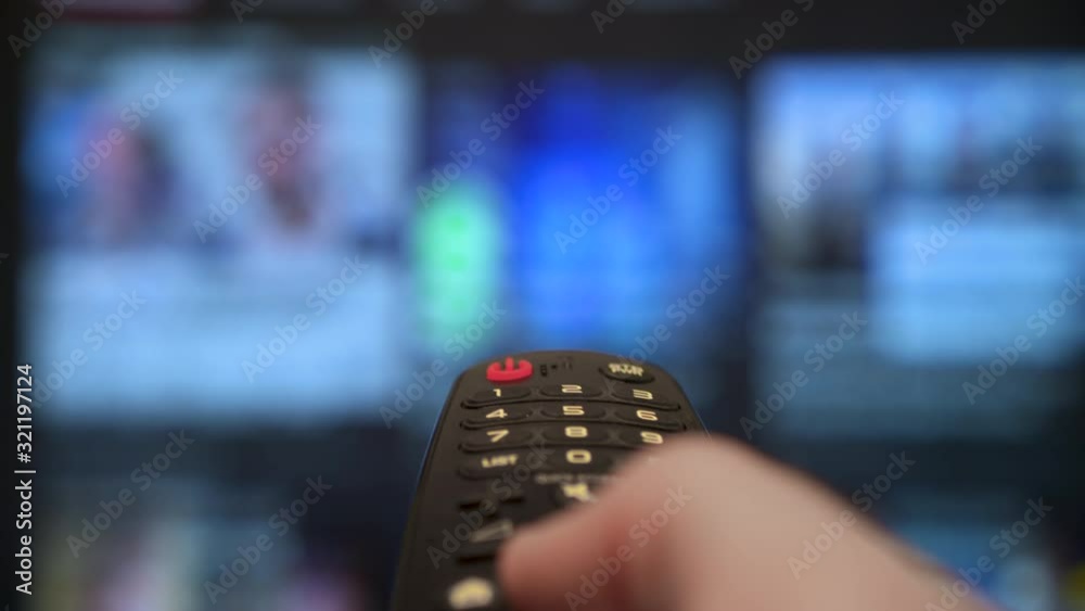 Male hand holding the TV remote control smart tv. Channel surfing, focused on the hand and remote control. Internet TV.