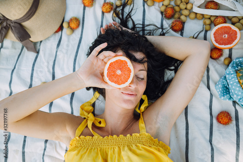 Woman covering her face with a grapefruit and lying on the blanket