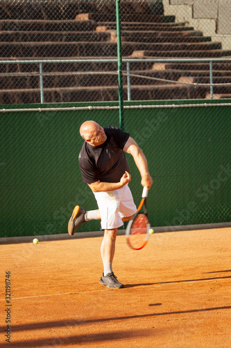 A bald man plays tennis on the court on a sunny day. Health and activity. Vertical. © Анна Демидова